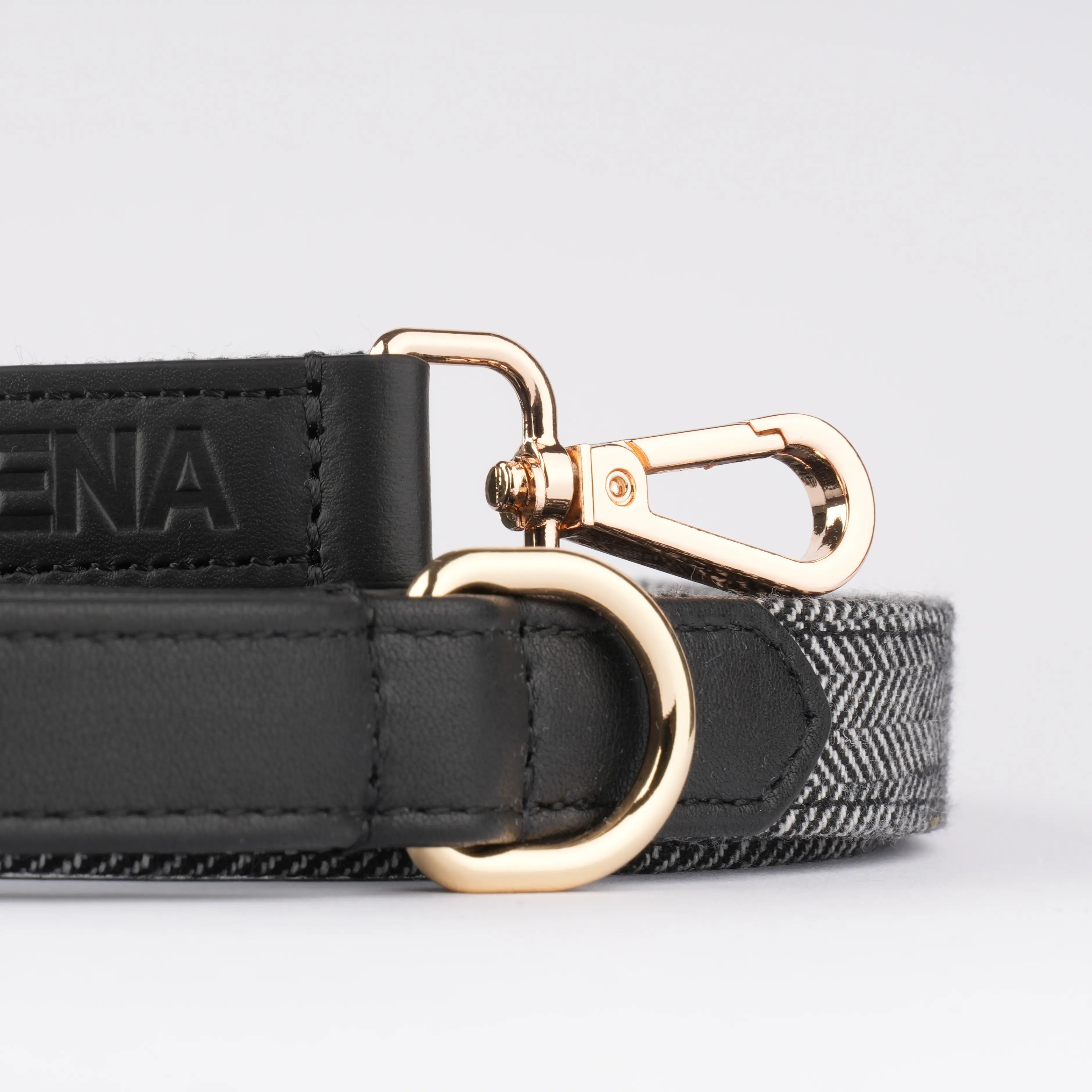 Schwarze Hundeleine mit Fischgrätstoff flach gerollt, Sicht auf Logo und goldene Metallteile